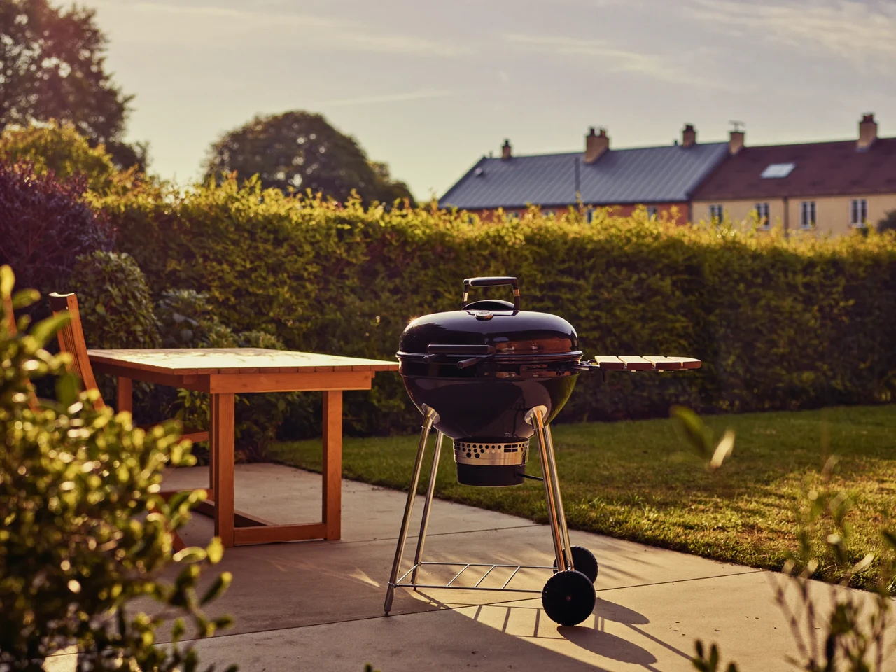 Dansk baghave i gyldent aftenlys med kulgrill, havebord og lav hæk