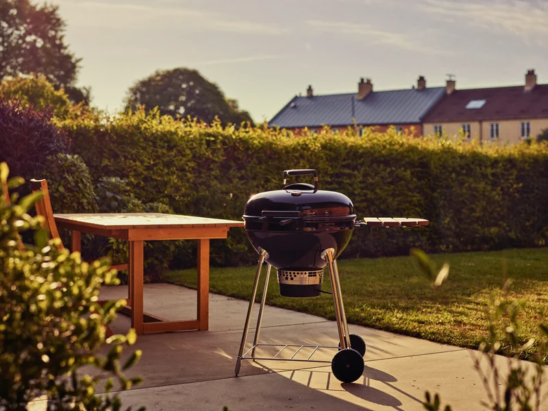 Dansk baghave i gyldent aftenlys med kulgrill, havebord og lav hæk