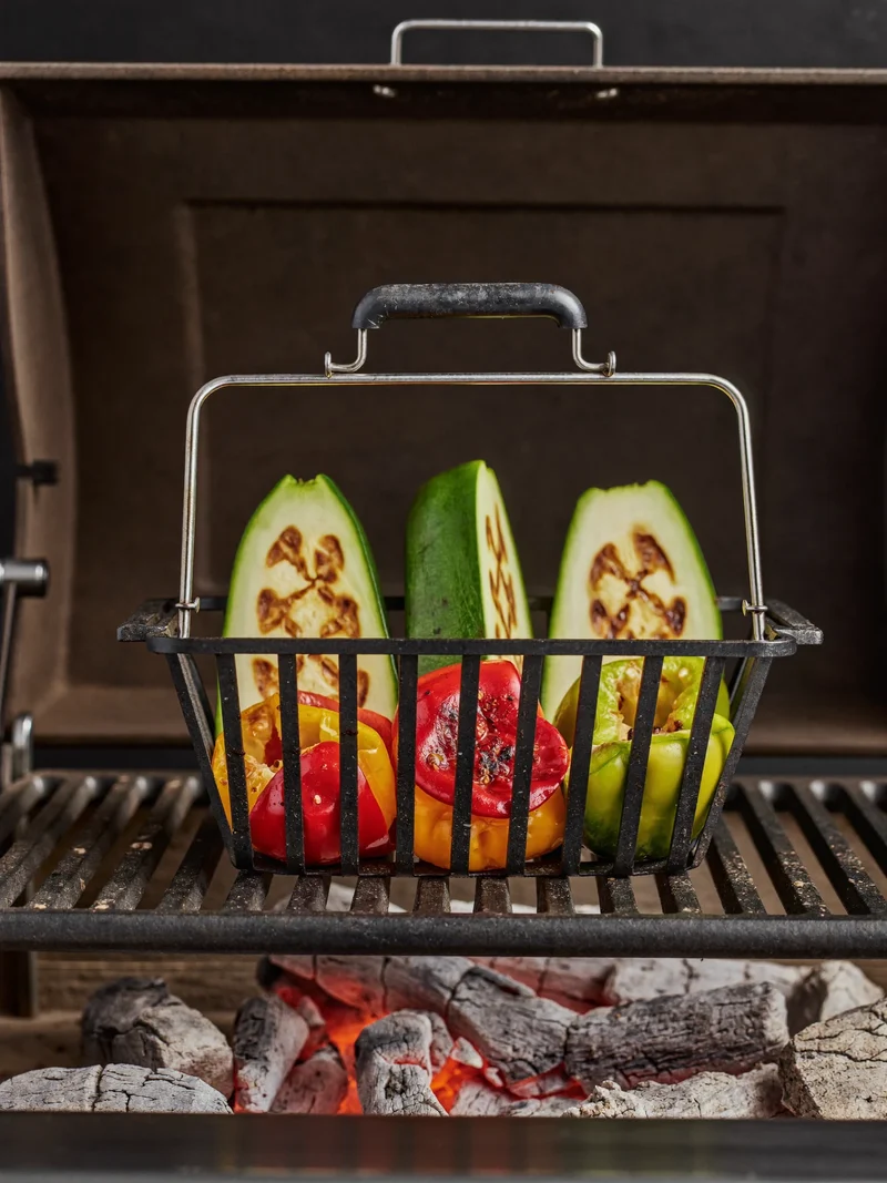 Støbejernsrist og grillkurv med peberfrugt og squash over klare gløder